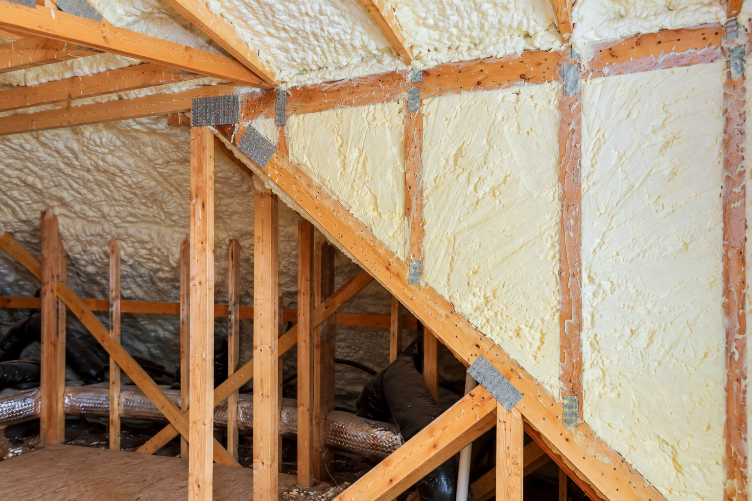 Attic framing coated with white spray foam insulation across the roof and wall surfaces.