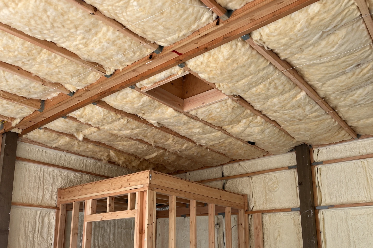 Fiberglass insulation fills the exposed rafters and wall framing of an attic.