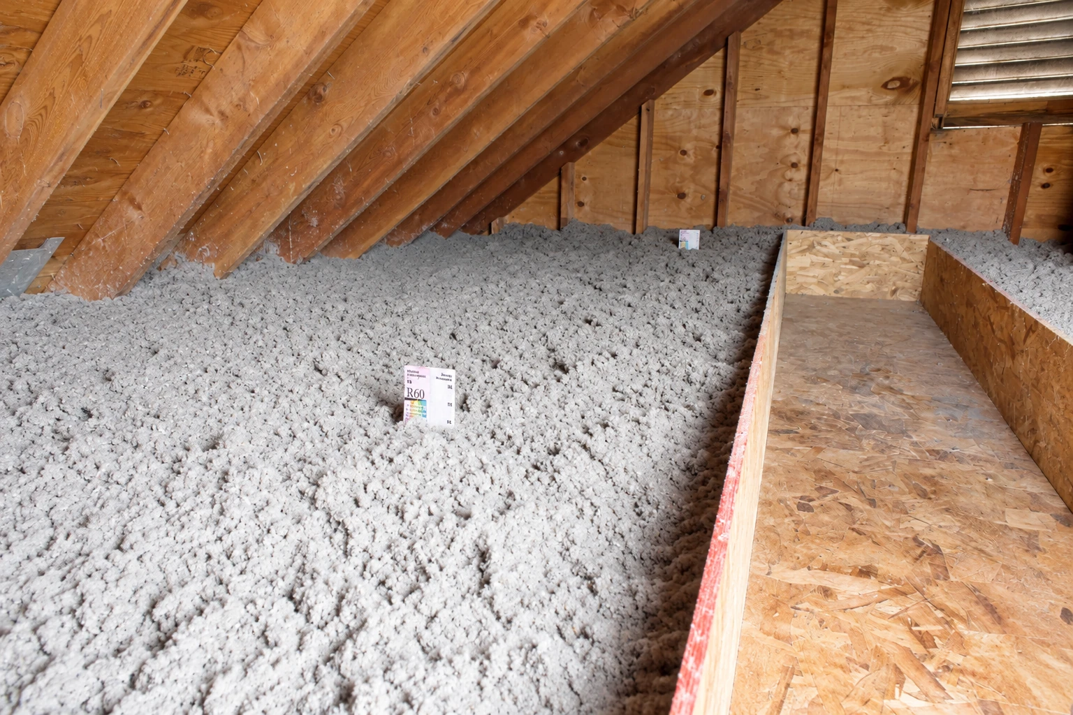 Gray blown-in insulation covers an attic floor beside a narrow raised plywood walkway.