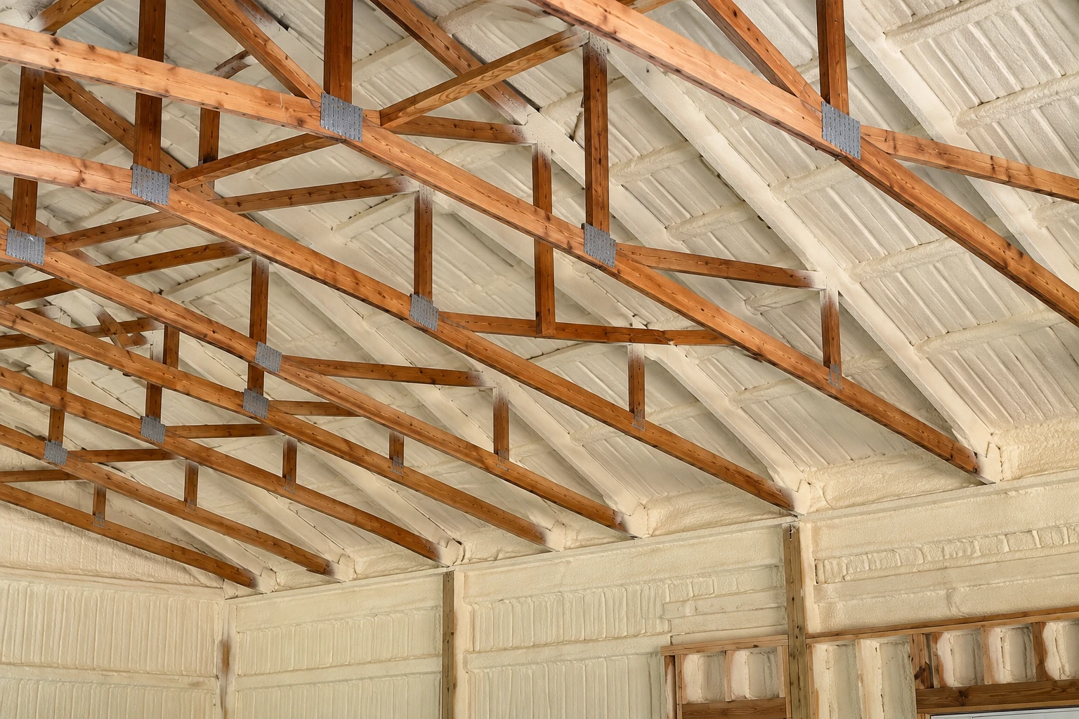 Cream spray foam coats a home's roof and walls between exposed wooden beams and trusses.